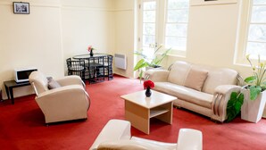 A living room with a red carpet, a beige sofa, a coffee table, and a small table with a vase of flowers. - Linaker Art Deco Motel (Beechworth)