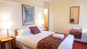A hotel room with a large bed, a bedside table with a lamp, a mirror, and a painting on the wall. - Linaker Art Deco Motel (Beechworth)