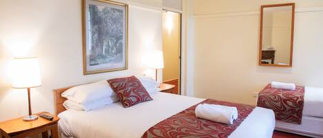 A hotel room with a large bed, a bedside table with a lamp, a mirror, and a painting on the wall.
