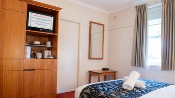 Habitación de hotel con una cama, un armario de madera, un televisor sobre el armario, una mesita y una ventana con cortinas.
