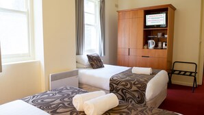 A hotel room with two beds, a wooden cabinet with a television, and a red carpet.