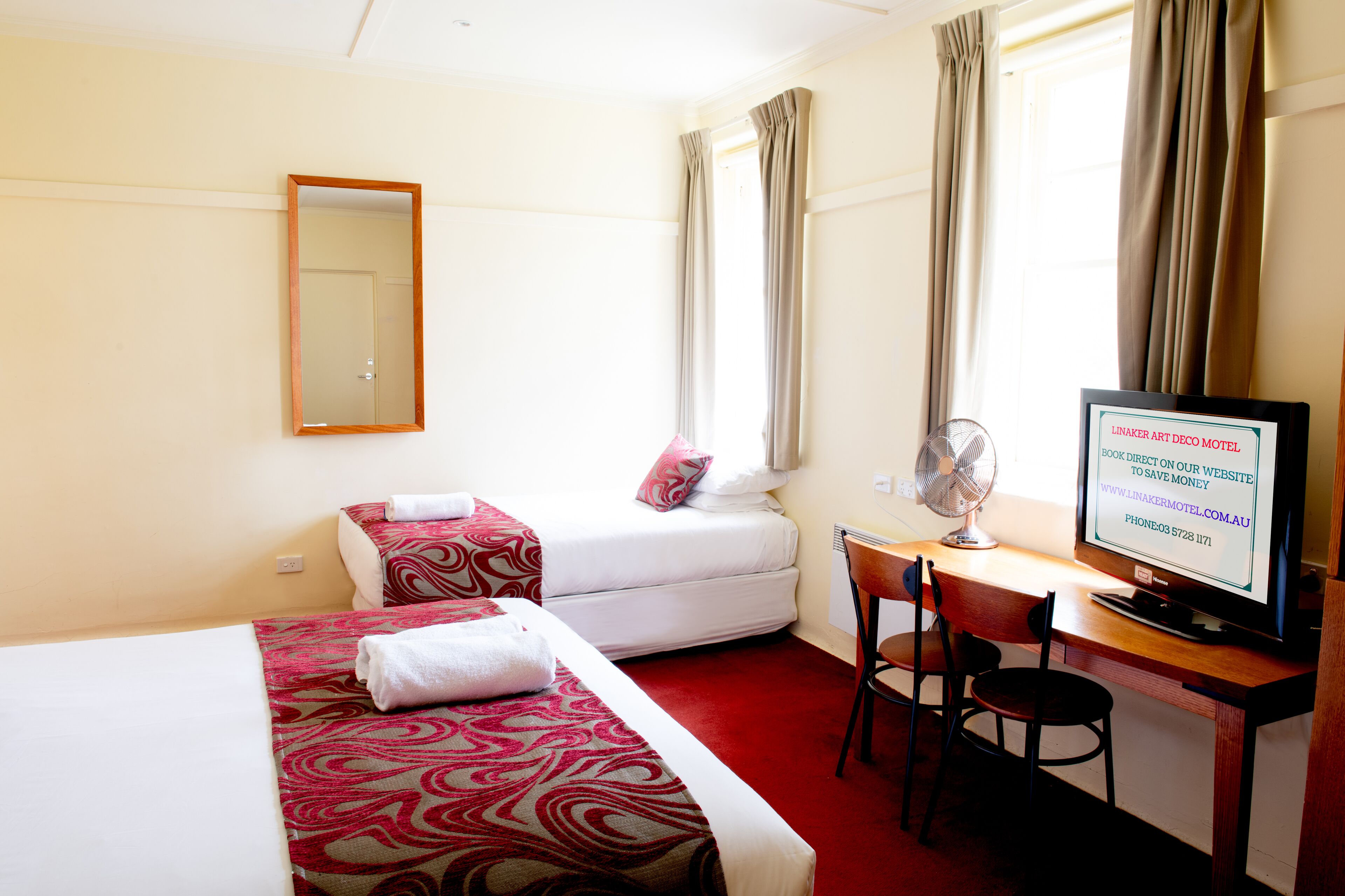 A hotel room with two beds, a desk with a computer, a chair, and a TV.