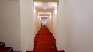 A hotel hallway with a red carpet, white walls, and a staircase on the left. - Linaker Art Deco Motel (Beechworth)