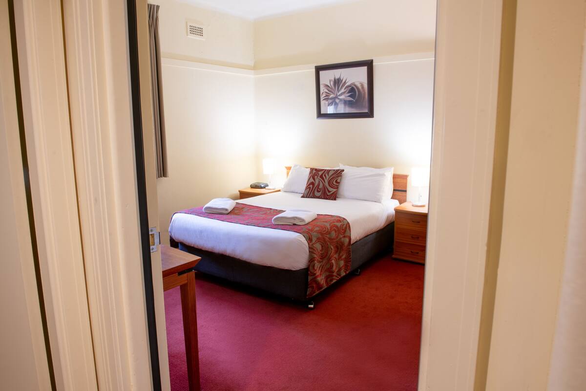 A hotel room with a bed, bedside table, and a nightstand.