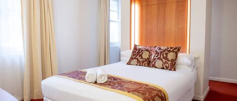 A hotel room with a large bed, a wooden headboard, and a red carpet.