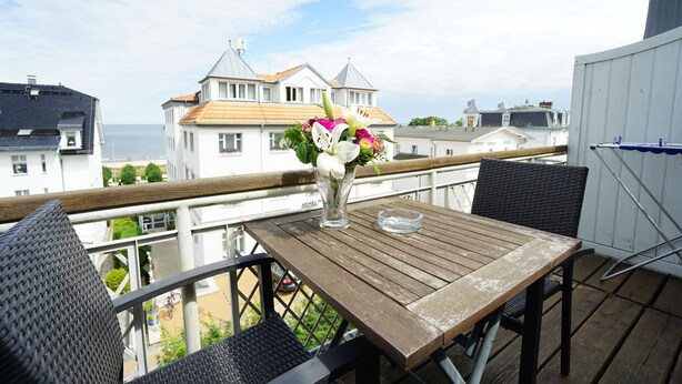 A wooden table with a vase of flowers on a balcony overlooking a residential area with houses and a body of water. - Villa Frieda with sea view - Whg. 11 (Heringsdorf)