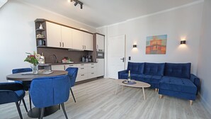 A modern living room with a blue sofa, a dining table with chairs, and a kitchen area with cabinets and appliances. - Villa Frieda with sea view - Whg. 11 (Heringsdorf)