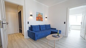 A modern living room with a blue sectional sofa, a round wooden coffee table, and two wall-mounted sconces. - Villa Frieda with sea view - Whg. 11 (Heringsdorf)