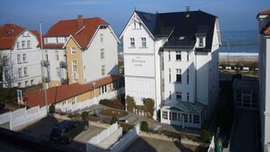 A row of white buildings with a red roof, a large white building with a sign, and a view of the sea. - Villa Frieda with sea view - Whg. 11 (Heringsdorf)