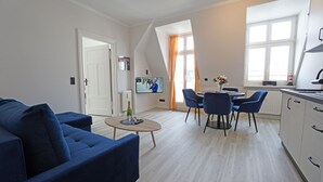 A modern living room with a blue sofa, a coffee table, and a dining area with chairs. - Villa Frieda with sea view - Whg. 11 (Heringsdorf)