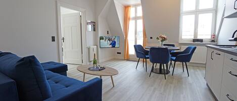 A modern living room with a blue sofa, a coffee table, and a dining area with chairs.