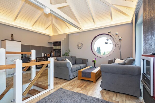 Ein großzügiger Wohnbereich mit hohen Decken, grauen Sofas, einem Holztisch und einem großen Fenster.