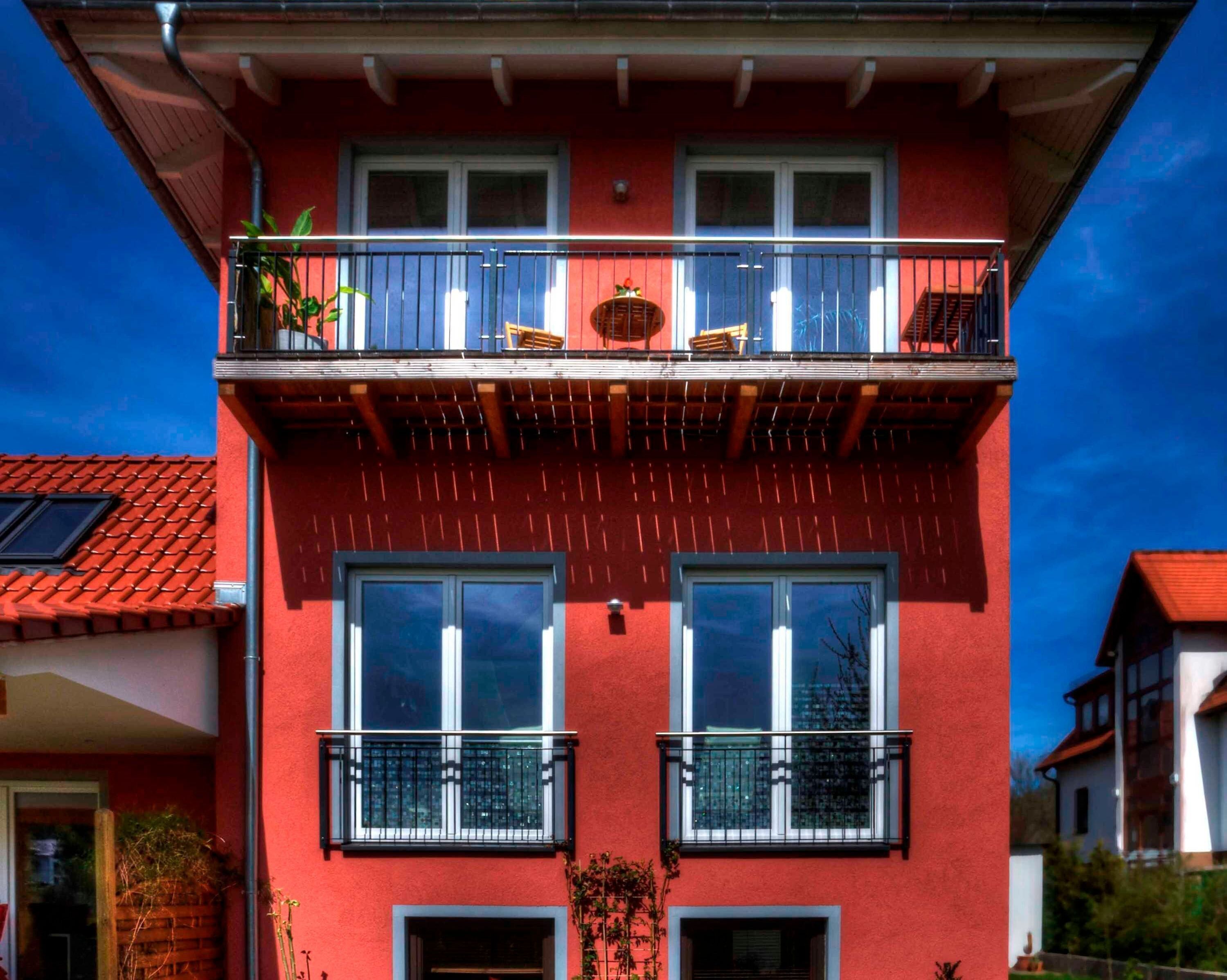 A red building with a balcony, two windows, and a door.