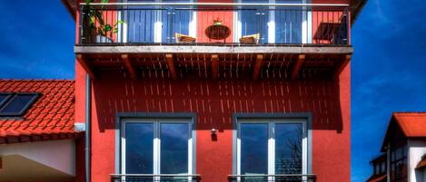 A red building with a balcony, two windows, and a door.
