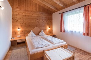 Een kamer met houten lambrisering, een bed, nachtkastjes en een raam met gordijnen.