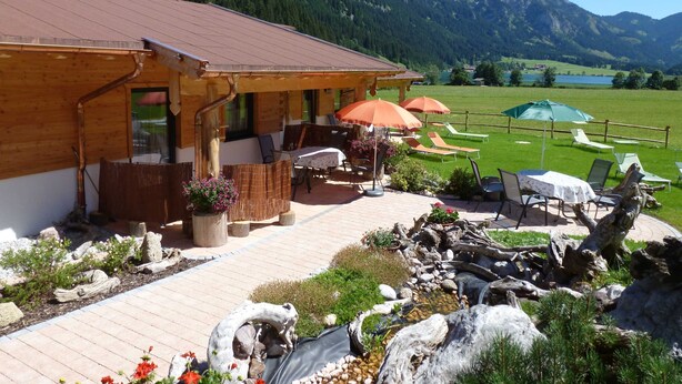 A wooden building with a patio area, outdoor seating, and a view of mountains. - Chalet Holiday House 12 - Almdorf Tirol (Haldensee)