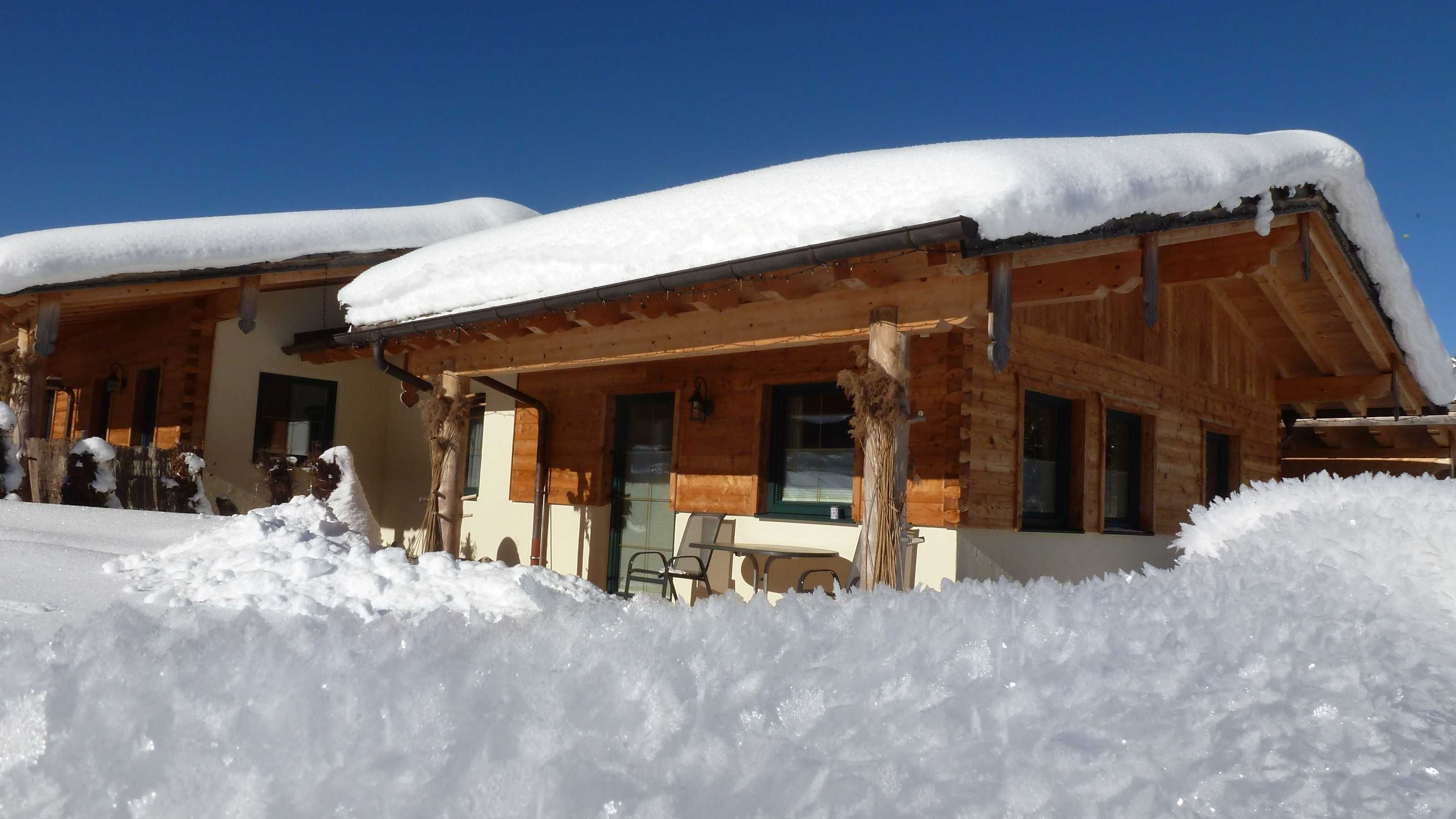 A wooden chalet with a covered porch and snow accumulation around the building.
