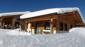 Een houten chalet met een overdekte veranda en sneeuw rond het gebouw.