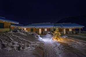 A snow-covered outdoor area with a Christmas tree and a building with multiple rooms and a covered patio.