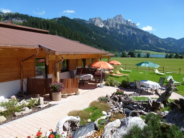 A wooden building with a patio area, outdoor seating, and a view of mountains.