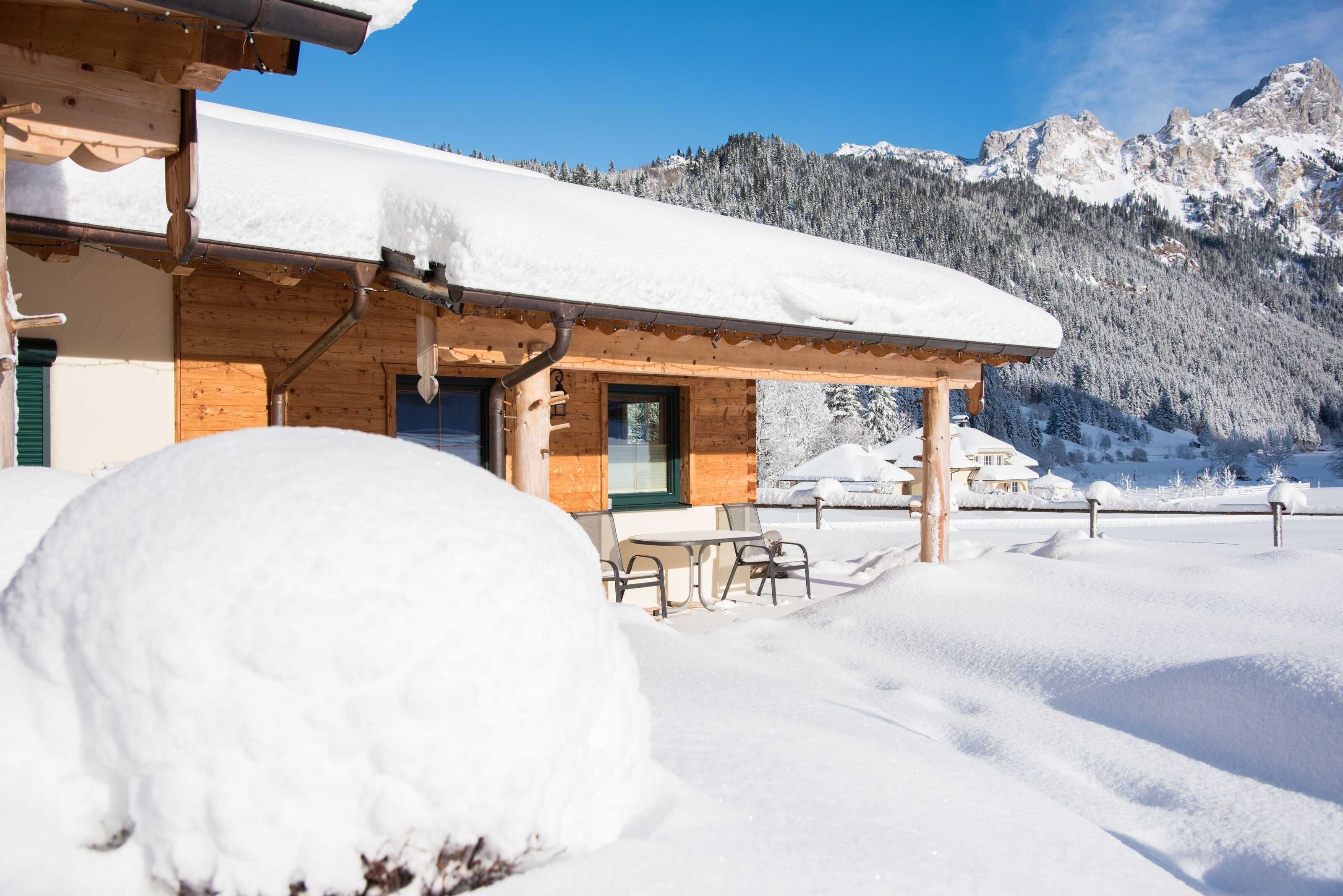 A wooden chalet with a snow-covered roof and a patio area with outdoor seating.