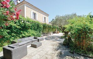 Une cour avec un sol en pierre, des meubles en osier et un bâtiment doté d’un toit en tuiles et de fenêtres.