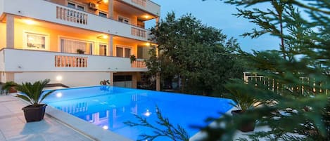 A multi-story building with balconies, a swimming pool, and potted plants.