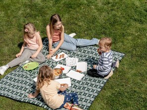 Vier Kinder sitzen auf einer karierten Decke draußen.