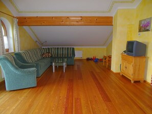 Una sala de estar con un sofá modular, una mesa de centro de vidrio, piso de madera, un mueble de madera y un televisor sobre un pedestal.