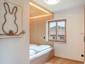 A bedroom with a bed, a window with a view, and a wooden ceiling.