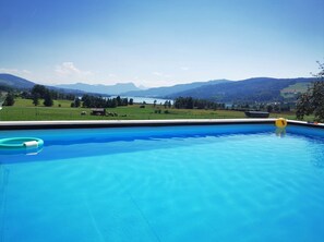 A swimming pool with a clear view of a lake and mountains in the background.