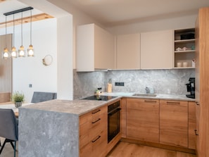A modern kitchen with a marble countertop, wooden cabinets, a built-in oven, and pendant lighting.
