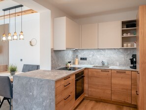 Una cocina moderna con encimera de mármol, armarios de madera, horno empotrado e iluminación colgante.
