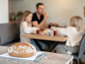 Una barra de pan sobre una tabla de cortar en un comedor con una mesa y sillas.