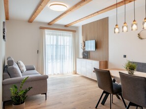 Un salon moderne avec un canapé, une table à manger et des chaises, des poutres en bois au plafond et un téléviseur fixé au mur.