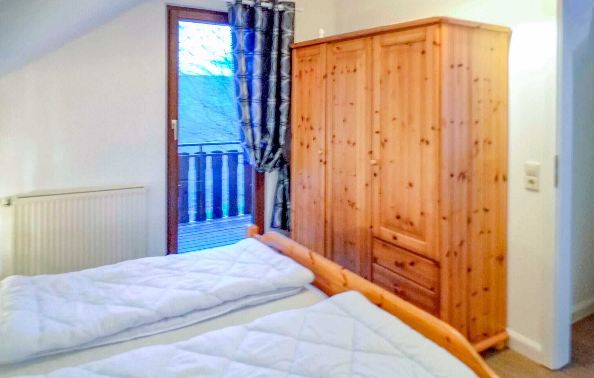 Ein Schlafzimmer mit zwei Betten, einem Holzschrank, einem Heizkörper und einer Tür, die auf einen Balkon führt.