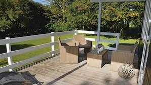 Eine Terrasse mit Korbmöbeln, einem kleinen Tisch und einem dekorativen Gegenstand.