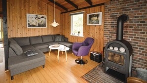 Ein gemütliches Wohnzimmer mit grauem Sofa, einem violetten Sessel, einem kleinen runden Tisch und einem Kaminofen.