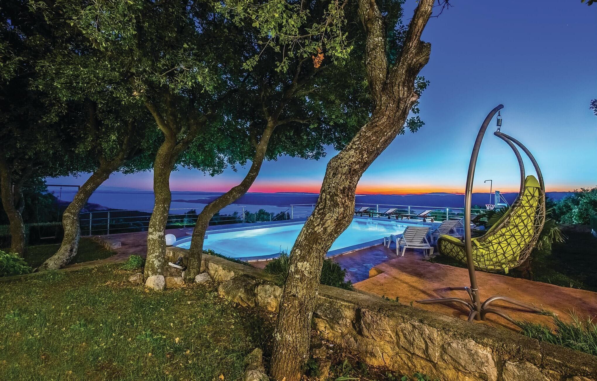 Un área de piscina con sillas de descanso y una hamaca, rodeada de árboles y con vistas panorámicas.