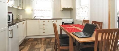 A compact kitchen with white cabinets, a stove, a microwave, and a dining table with chairs.
