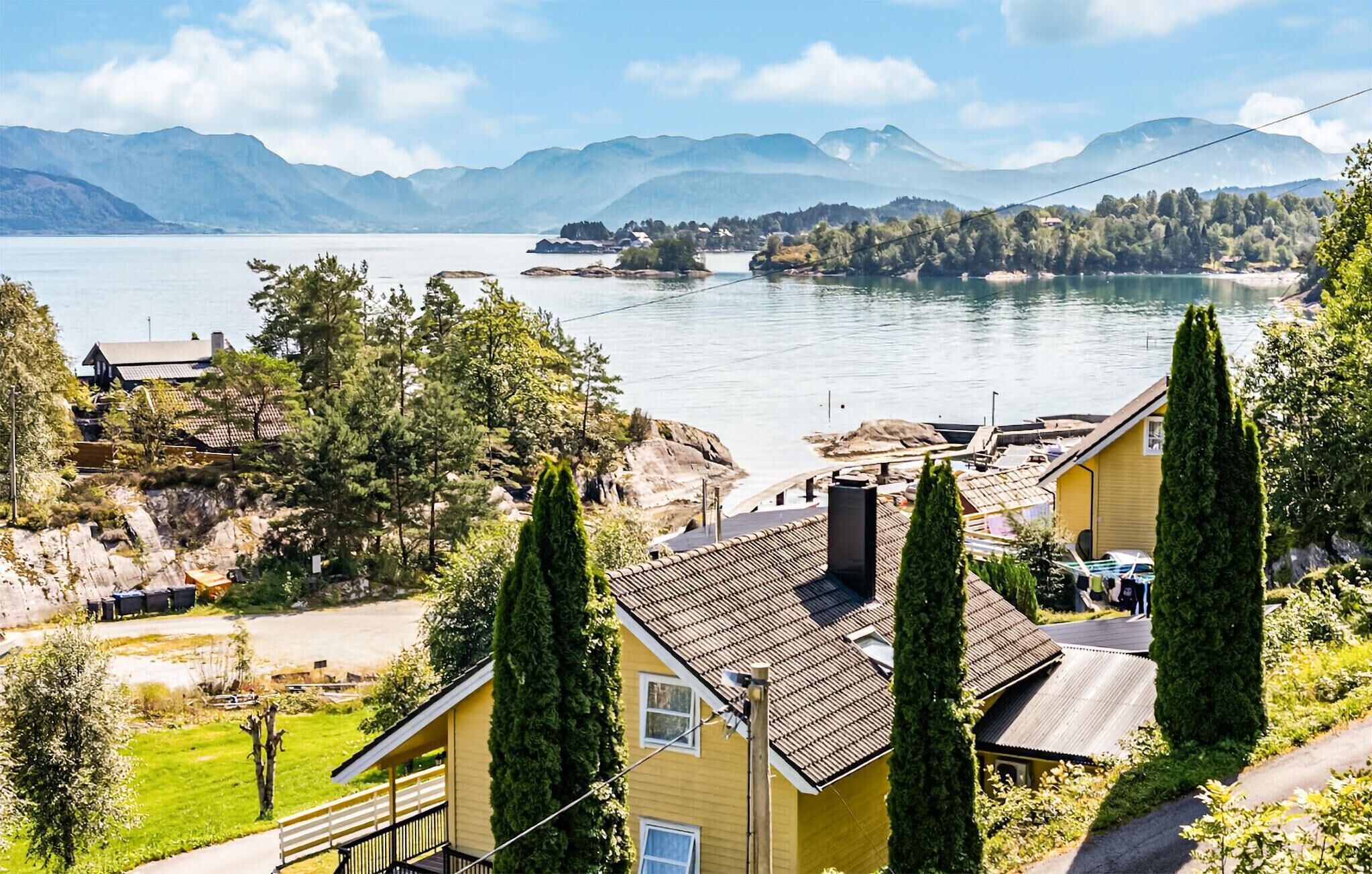 Una propiedad junto al lago con una casa amarilla, un muelle y montañas al fondo.