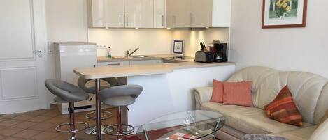 Un espacio habitable compacto con kitchenette, una mesa de vidrio para comer, un sofá y una cafetera.
