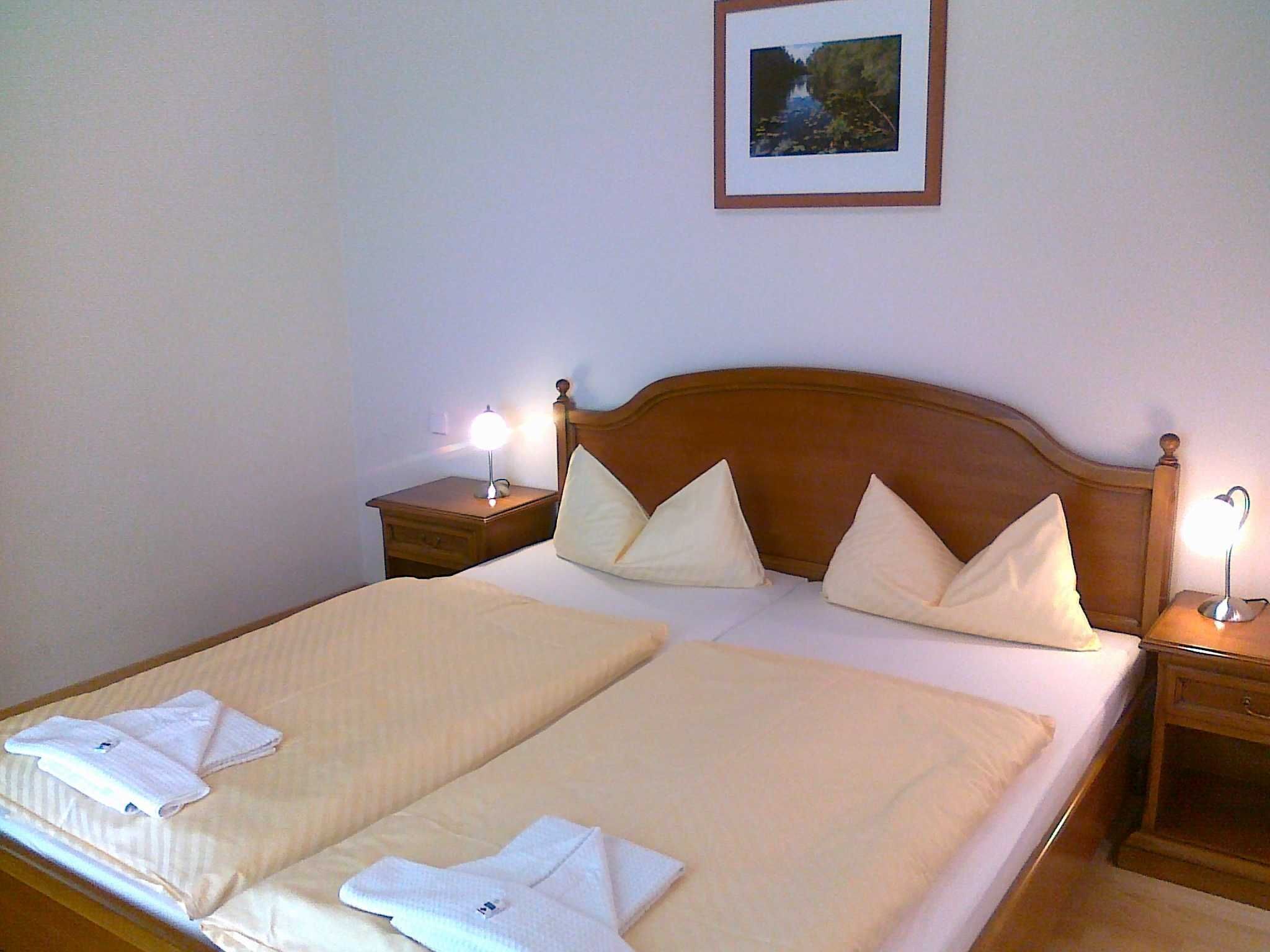 A double bed with two pillows, a bedside table with a lamp, and a framed picture on the wall.