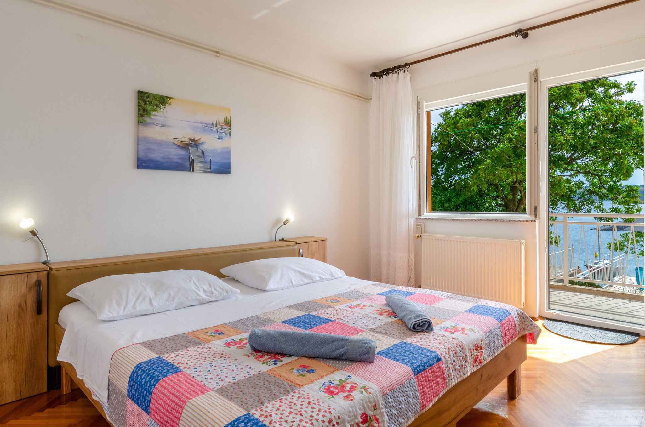 Quarto com cama de madeira, colcha, pintura na parede e varanda com vista.