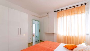 Une chambre avec un grand lit, une armoire blanche et une vue sur un couloir.
