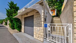 Un bâtiment en pierre doté d’une entrée fermée par un portail, d’un balcon couvert et d’une enseigne bleue indiquant qu’il s’agit d’un immeuble d’appartements.