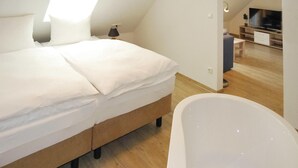 Un dormitorio con cama, mesita de noche, lámpara, televisor y baño con bañera.