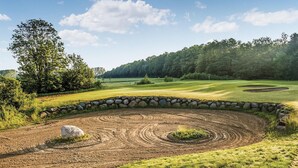 Un campo de golf con un muro de piedra, un árbol grande y cielo despejado.
