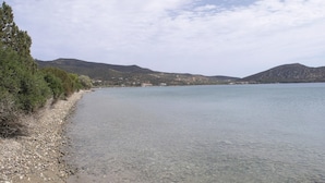 On aperçoit clairement une plage bordée d’une côte rocheuse, avec une eau calme et des collines à l’horizon.