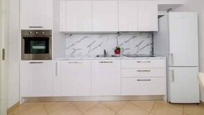 A modern kitchen with white cabinets, a built-in oven, a marble backsplash, and a white refrigerator. - Holiday apartment with terrace and sea view (Crikvenica)